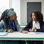 Black educator working with multiracial student in classroom.