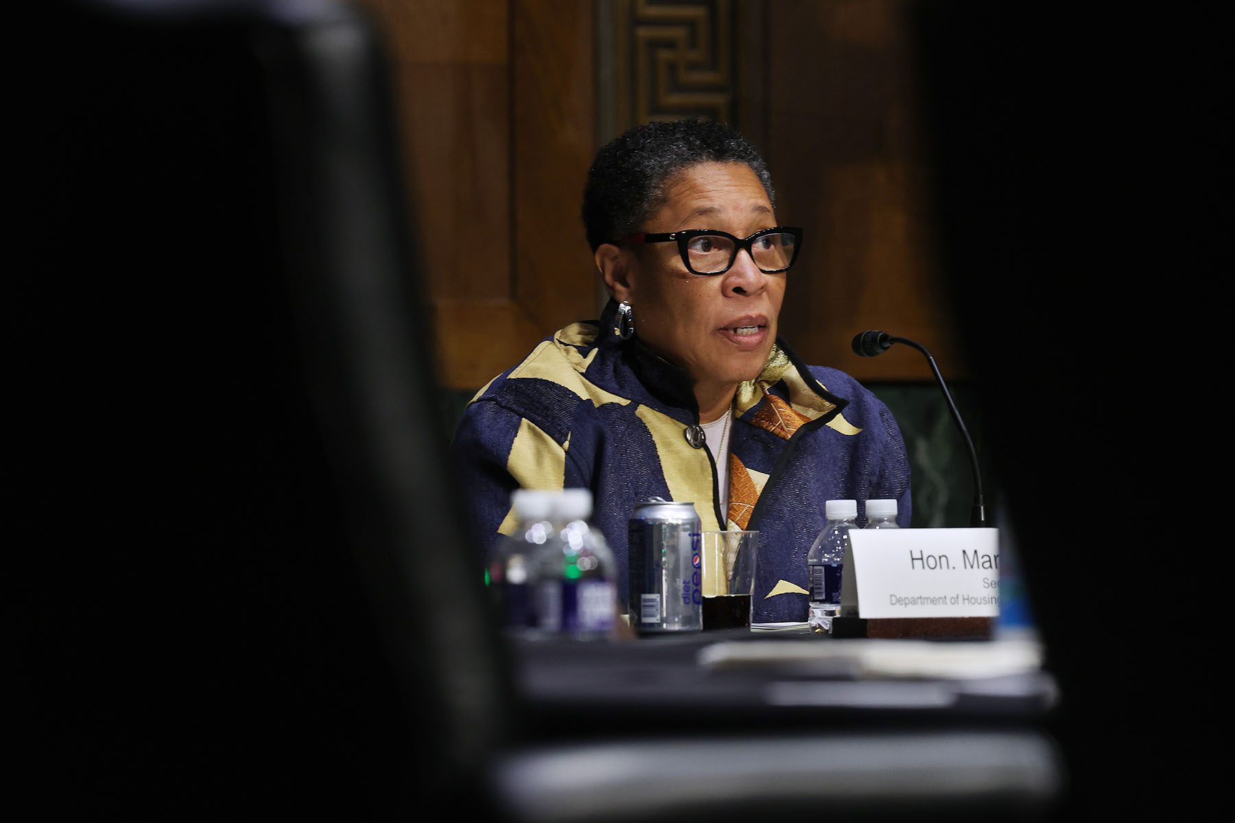 Marcia Fudge speaks into a microphone. She is framed by two empty seats in the foreground.
