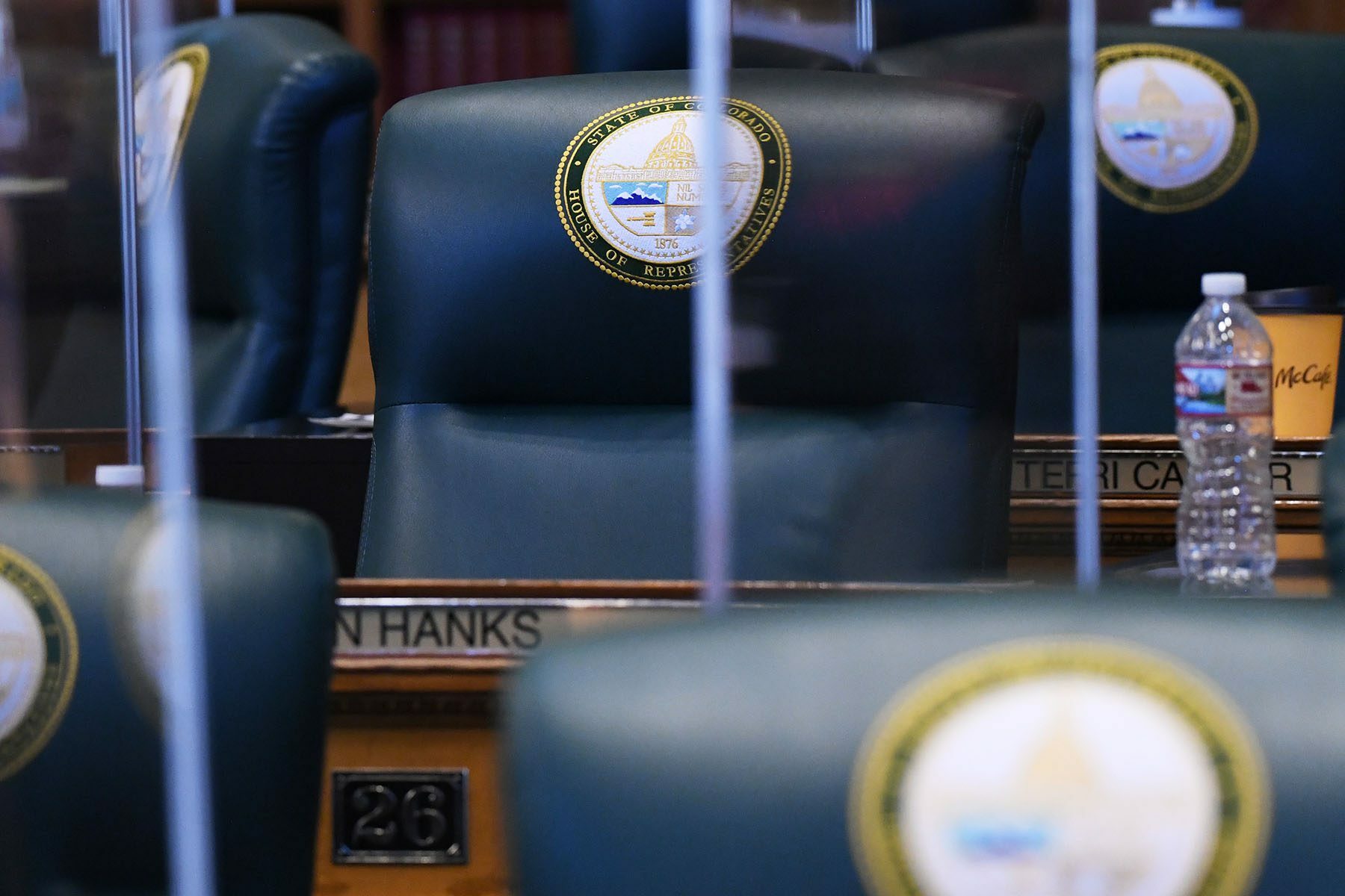 Empty desks and desk chairs are seen at the Colorado State Capitol. The chair are engraved with a 
