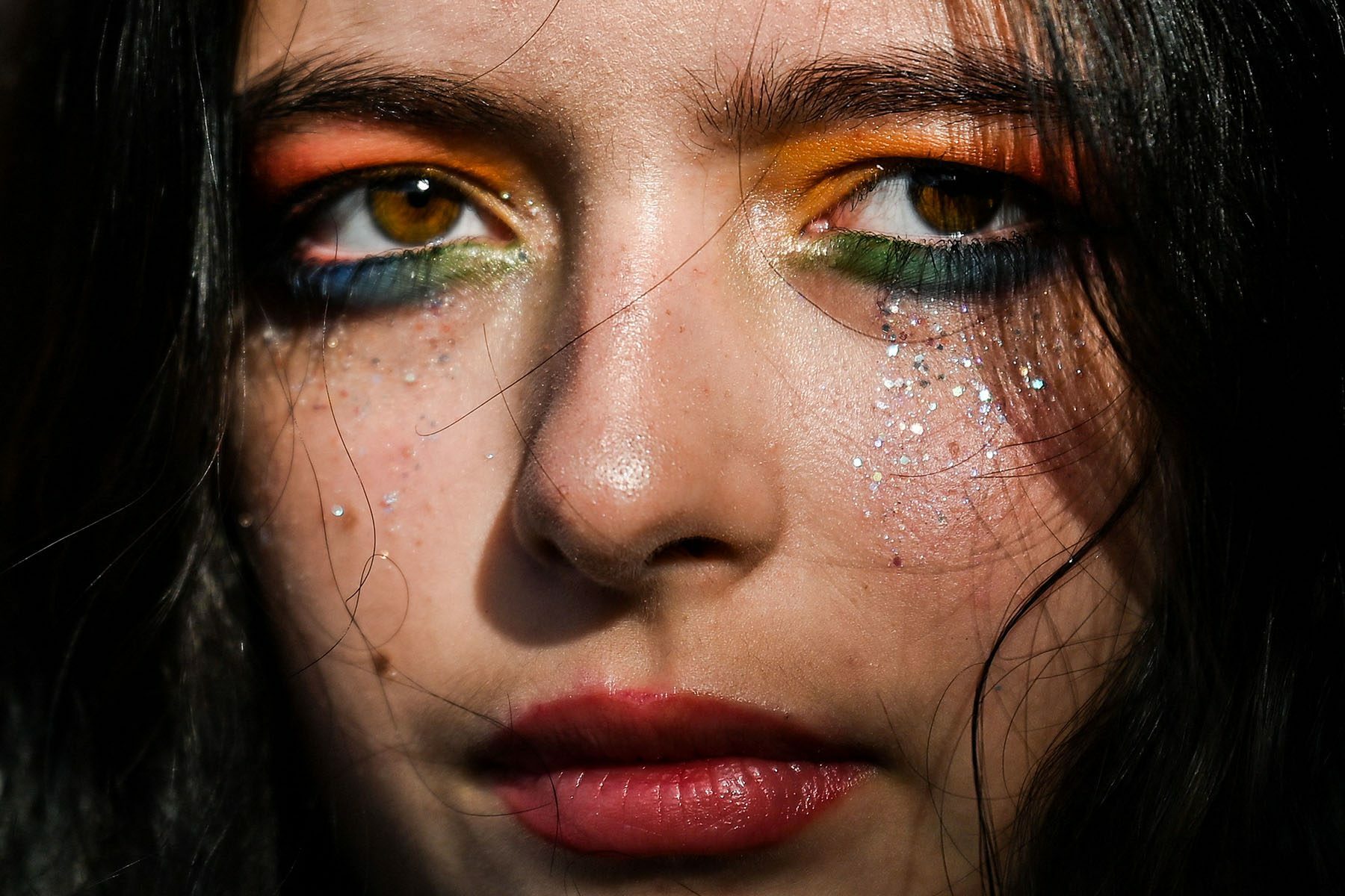 A close up of a person with rainbow colored eye makeup and glitter tears.