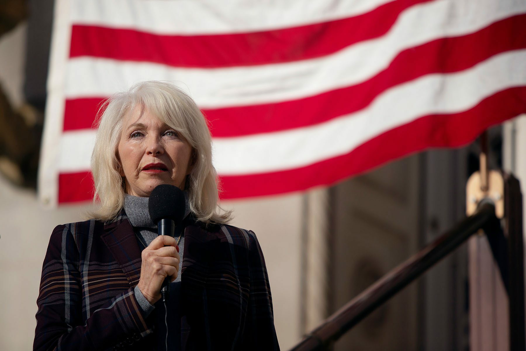 Tina Peters speaks into a microphone. An American flag can be seen in the background.