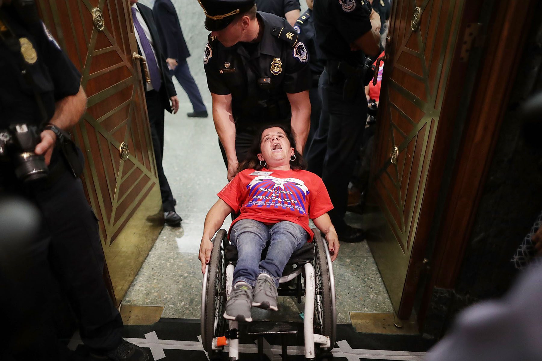A woman in a wheelchair appears to yell out as a Capitol policeman drags her wheelchair out of a room.