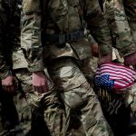 Soldiers holding american flag walk together in a tight group.