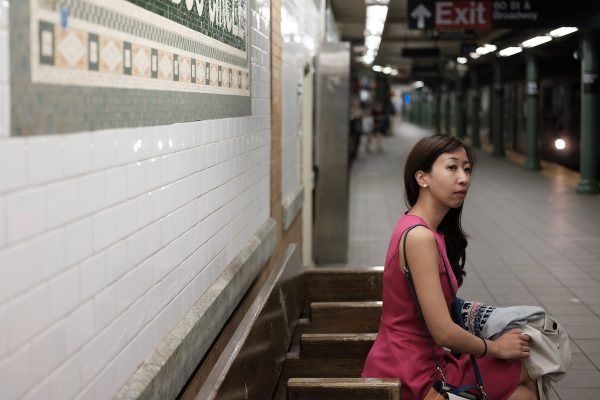 An asian woman in a pink dress waits for the subway in New York City.