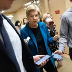 Sen. Elizabeth Warren walks down a corridor flanked by reporters.