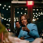 Val Demings sitting at a table with members of the Cuban-American community at a restaurant and gesturing while she speaks.