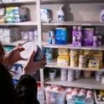 Katie Wussler checks the lot number under a can of baby formula in a storage closet containing baby supplies.