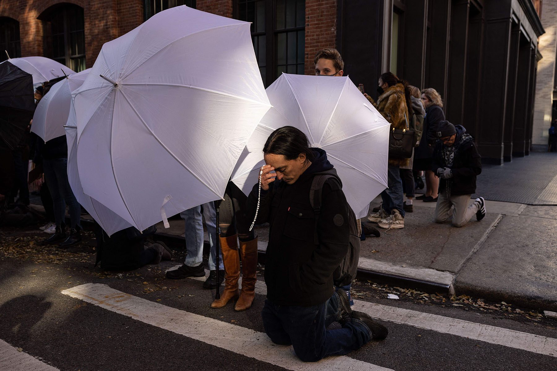 An anti-abortion activist kneels on the street in prayer in front of Planned Parenthood - Manhattan Health Center while abortion rights activists block the clinic using white umbrellas.