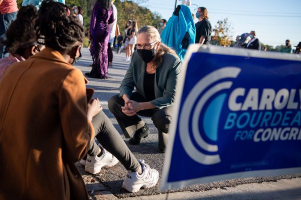 Carolyn Bourdeaux kneels to speak to supporters sitting on a curb. A sign that reads 