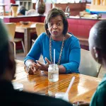 Cheri Beasley sits at a table with the owners of a Durham based Zimbabwean restaurant.