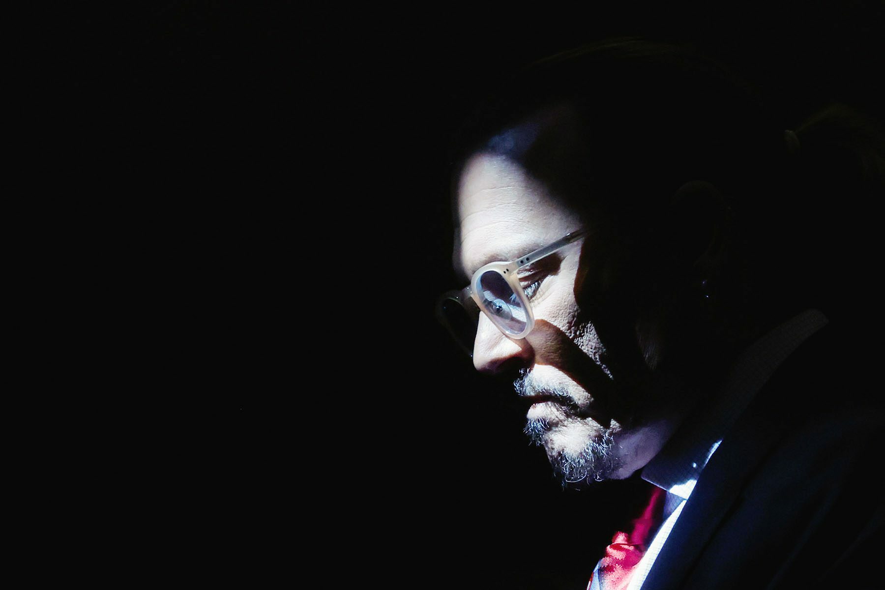 Johnny Depp's face is illuminated by sunlight while the rest of the image is dark. He is looking down and wears a solemn expression on his face.