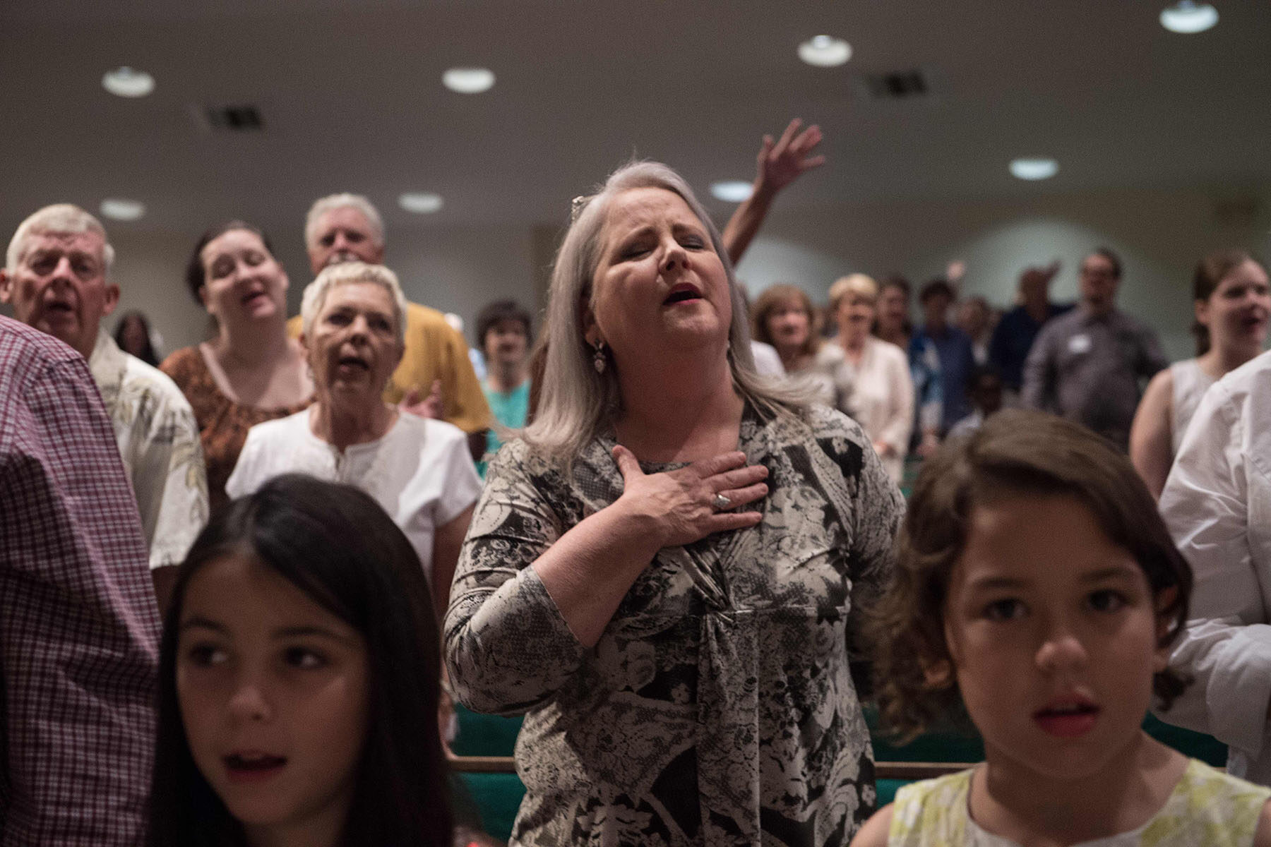Christian evangelicals gesture and pray during a church service. Two young children are in the foreground of the image. One is looking at the camera, the other is looking away.