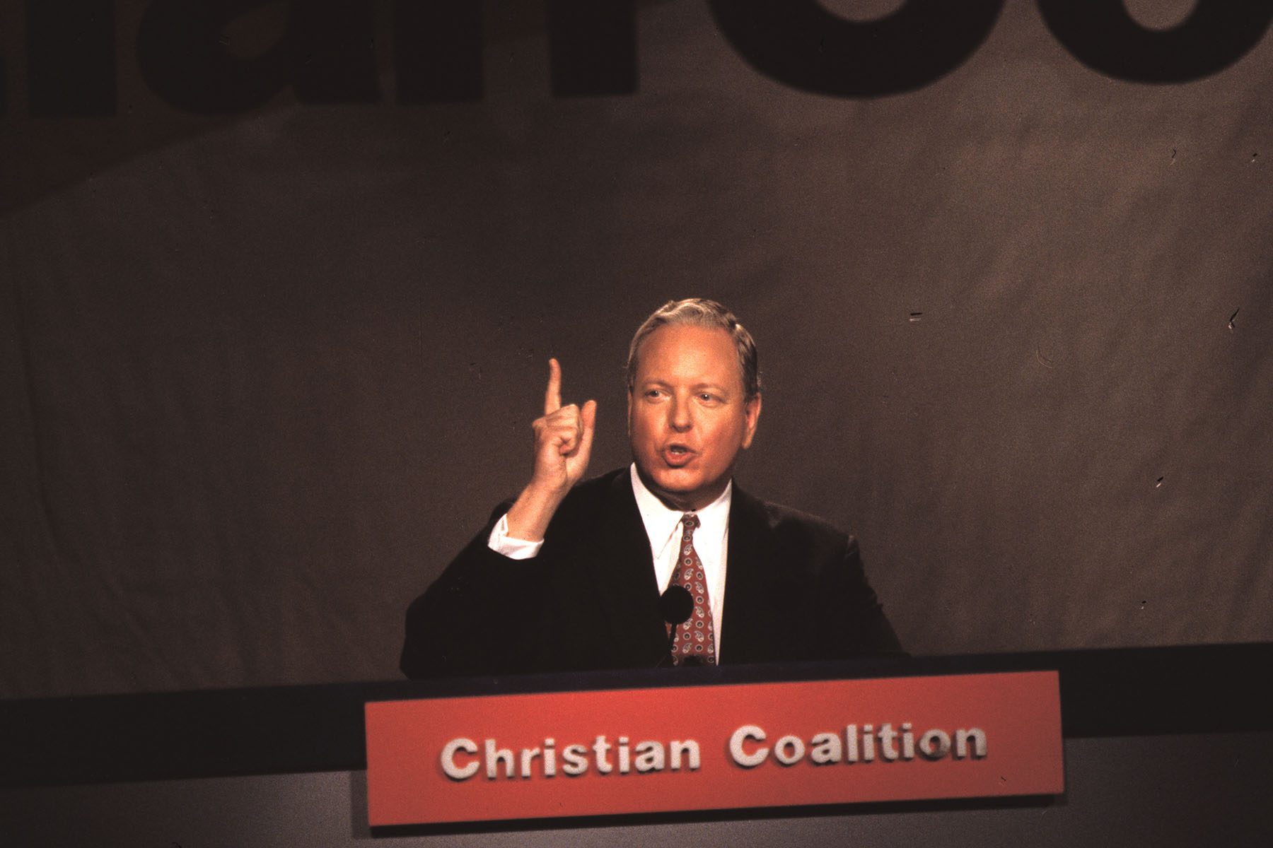 Paul Weyrich delivers a speech at a podium on which is written "Christian Coalition."