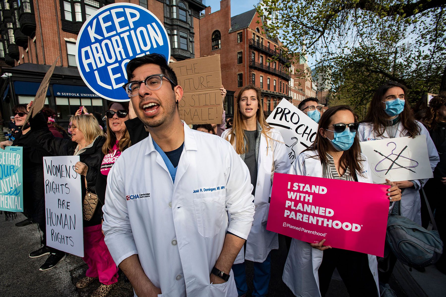 A group of doctors and medical workers join protesters. They hold signs that read "I stand with planned parenthood," "keep abortion legal," and "women's rights are human rights."
