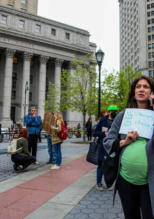 A visibly pregnant person holds a sign that reads 