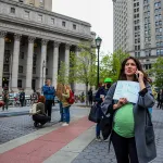 A visibly pregnant person holds a sign that reads 