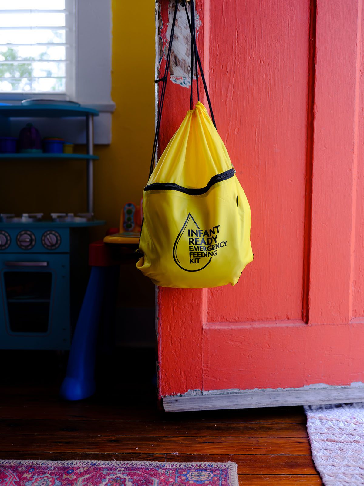 An infant ready emergency feeding kit hangs on a door at Malaika Ludman's home. The kit is a yellow bag with a zipper.