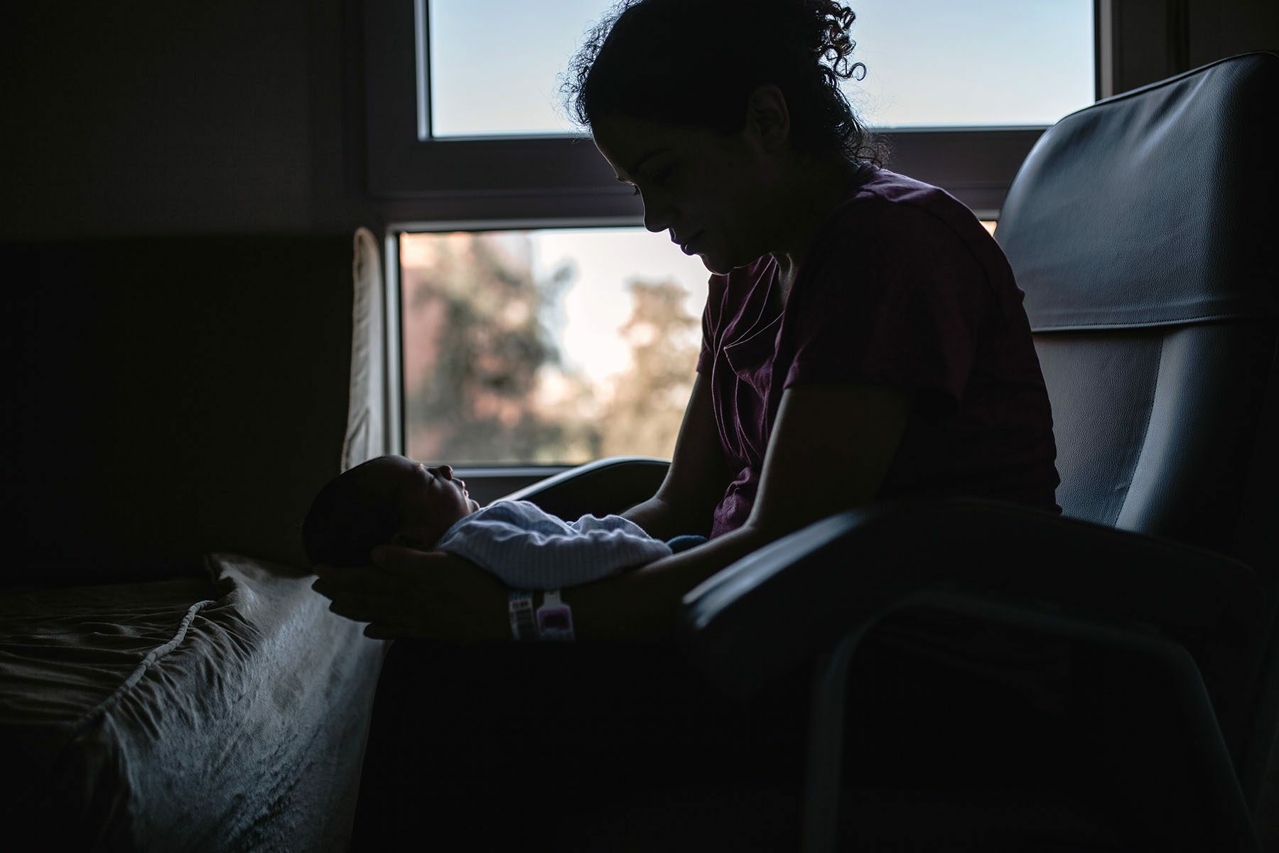 Silhouette of Woman Holding Newborn Son While Sitting On Chair In a Hospital