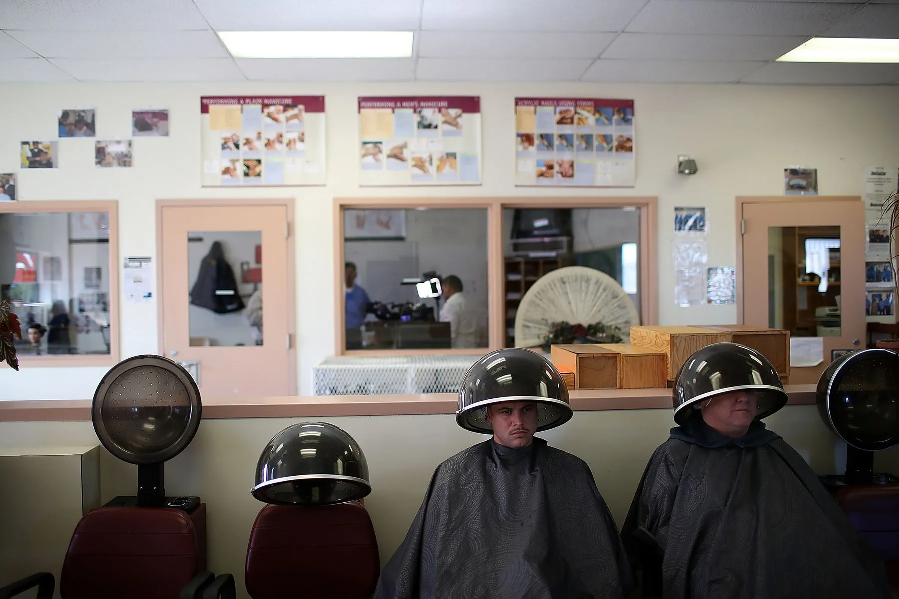 Inmates sit under hood dryers during a cosmetology class.