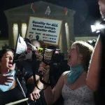 A person yells into a megaphone, as other demonstrators join in, in front of the U.S. Supreme Court