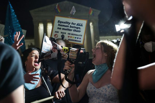 A person yells into a megaphone, as other demonstrators join in, in front of the U.S. Supreme Court