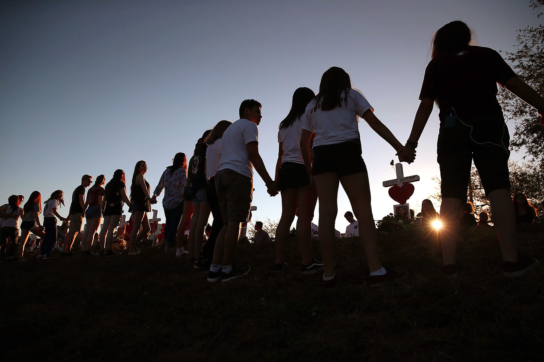 Students and family members holds hands around a makeshift memorial in front of Marjory Stoneman Douglas High School.