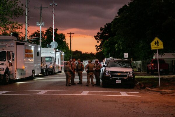 Law enforcement officers speak together outside of Robb Elementary School in the evening. The colors of the sunset are reflected on the street.