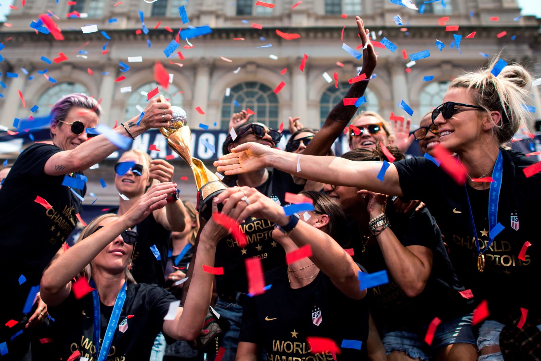 Players reach for the World Cup as confetti rains on them during a parade.