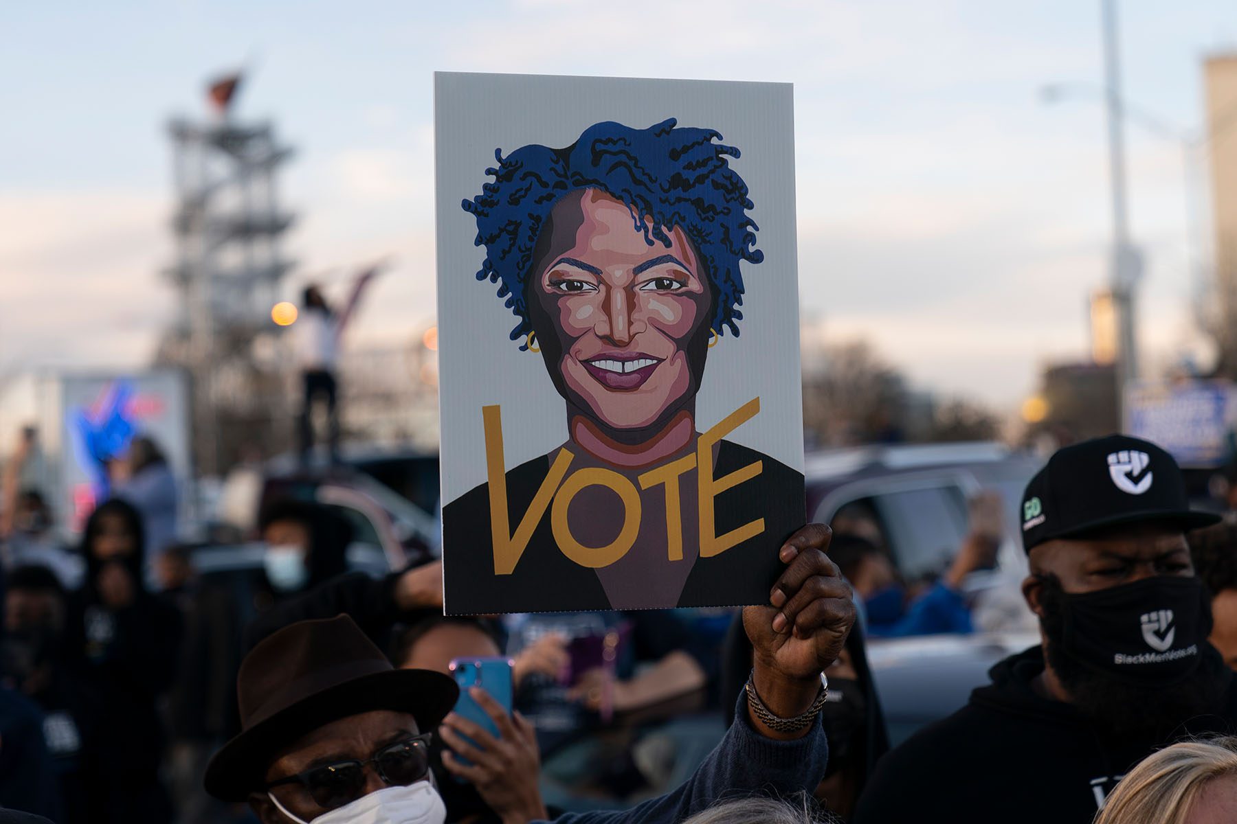 People in the crowd hold up an image of Stacey Abrams that reads "VOTE."