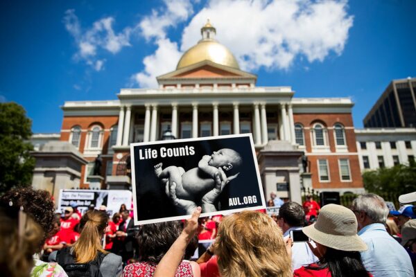 Anti-abortion demonstrators are seen in front of the Massachusetts Statehouse. In the foreground, a protester holds a signs on which an image of a baby is printed with the words 