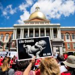Anti-abortion demonstrators are seen in front of the Massachusetts Statehouse. In the foreground, a protester holds a signs on which an image of a baby is printed with the words 