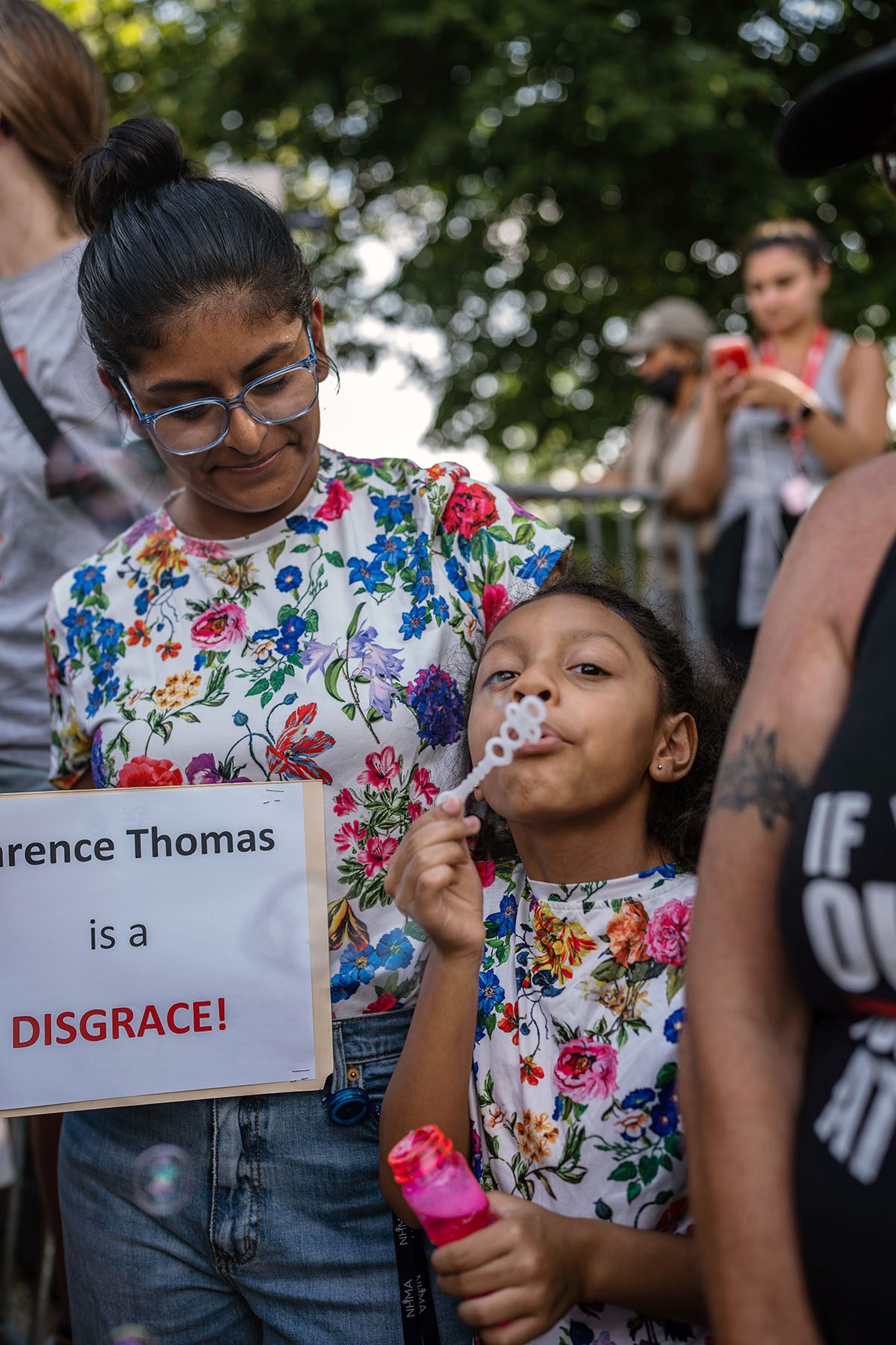 Jocelyn Canas poses with daughter Olive Nemorin, 9, as she blows soap bubbles. Jocelyn Canas holds a sign that reads "Clarence Thomas is a Disgrace!"
