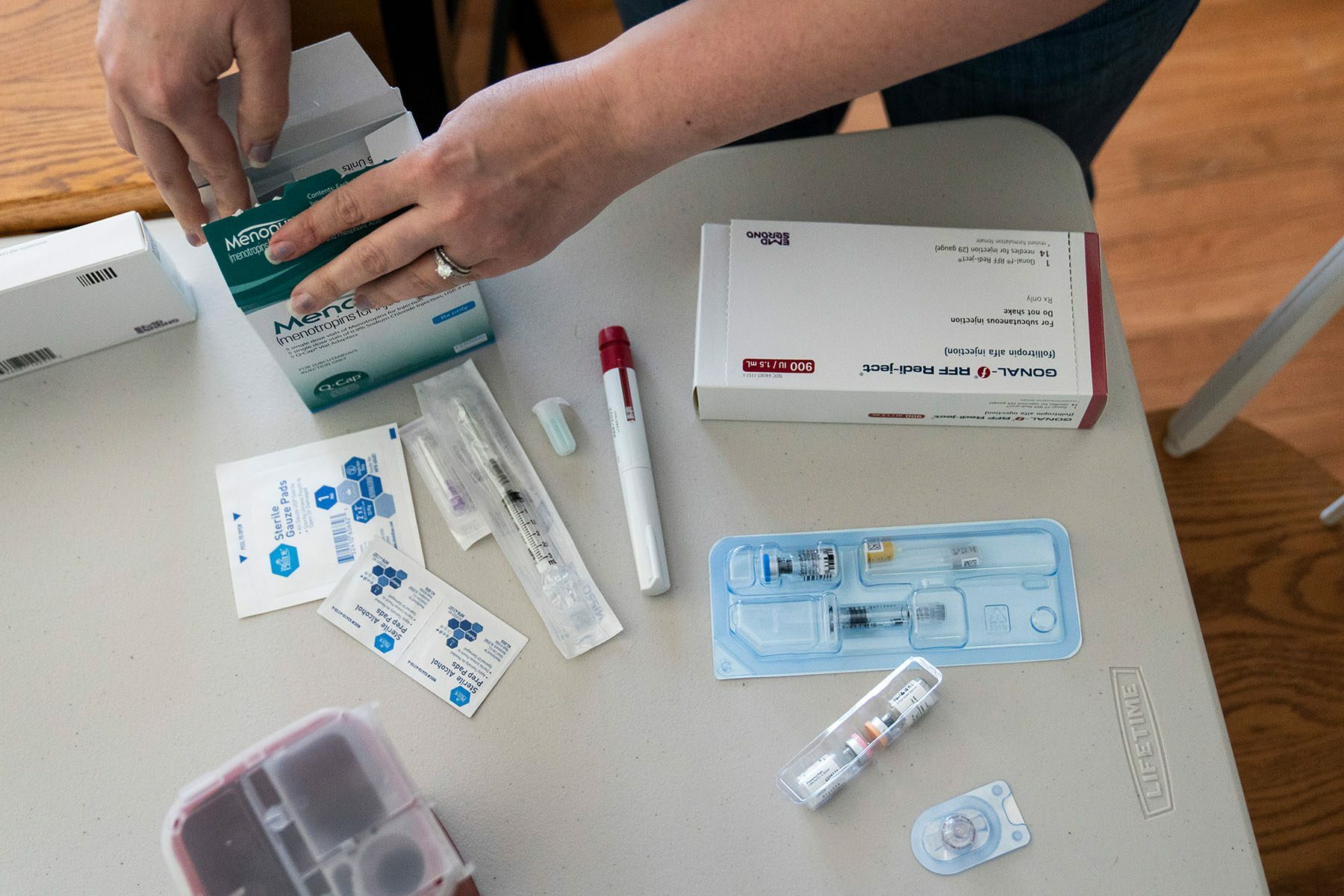 A woman goes through her IVF medications at home. Several boxes of medication and needs are seen on the table.