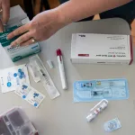 A woman goes through her IVF medications at home. Several boxes of medication and needs are seen on the table.