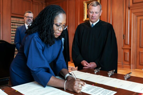 Chief Justice John G. Roberts, Jr. looks on as Justice Ketanji Brown Jackson signs the Oaths of Office in the Justices' Conference Room.