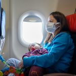 Young Woman traveling with her baby by plane wearing a face mask.
