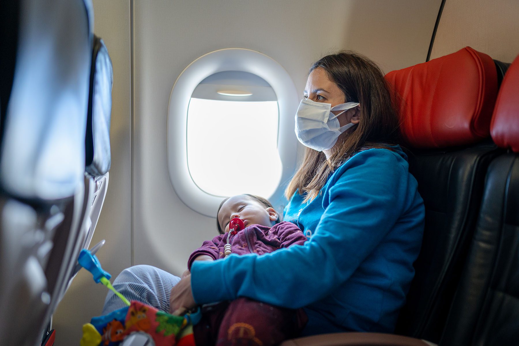 Young Woman traveling with her baby by plane wearing a face mask.