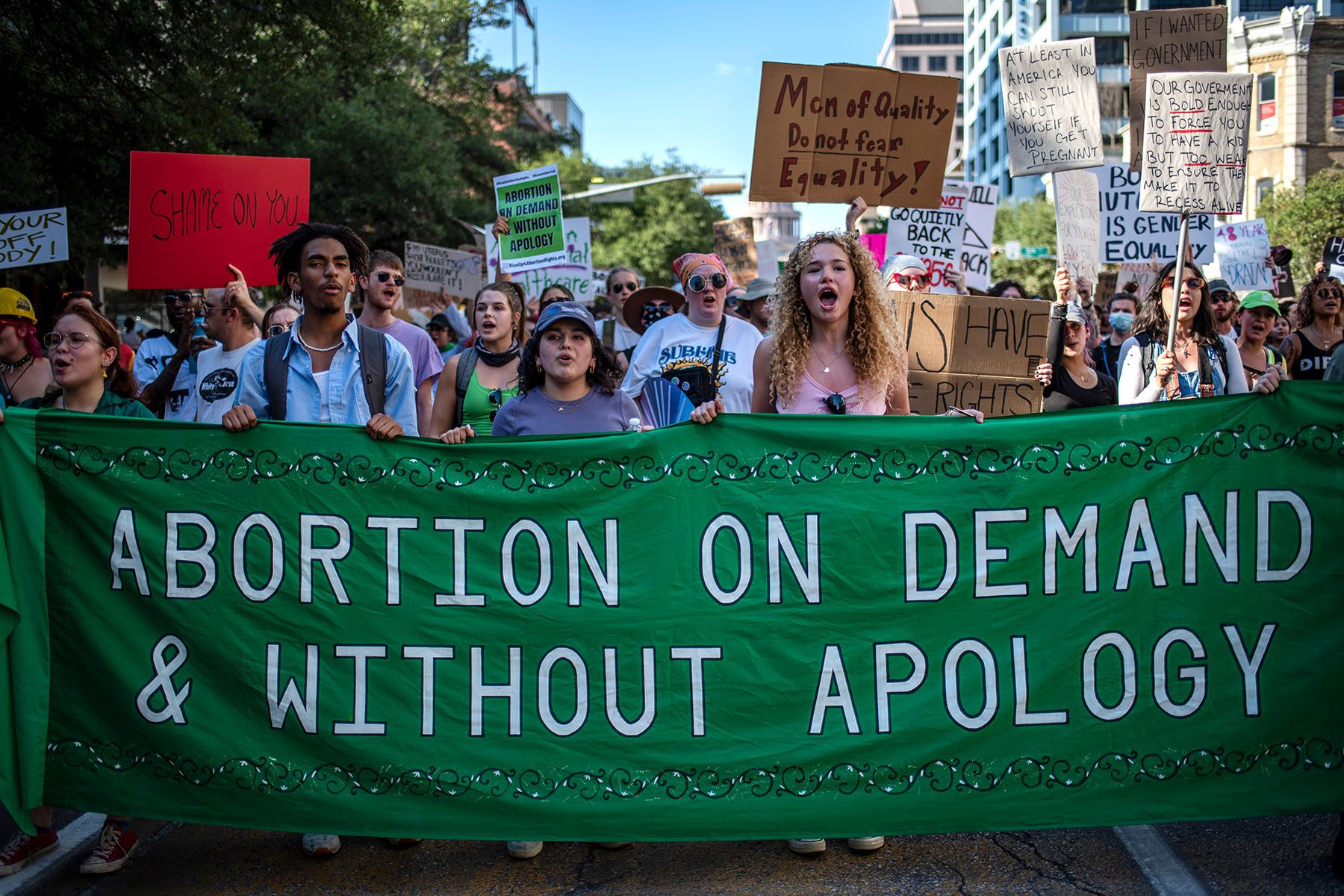 Protesters march while holding signs during an abortion-rights rally. A large banner reads 