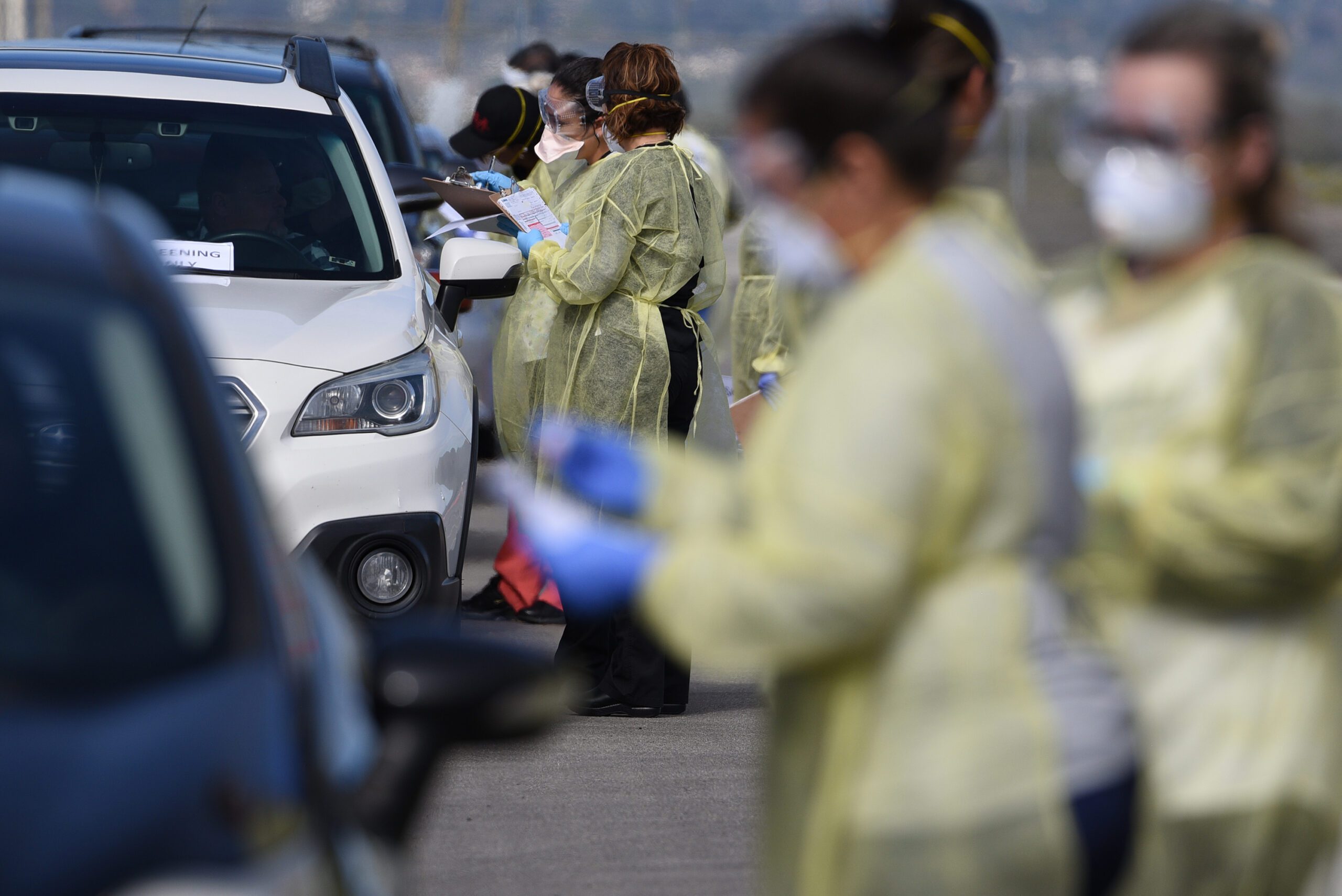 Medical personnel administer drive-thru COVID tests in a parking lot.