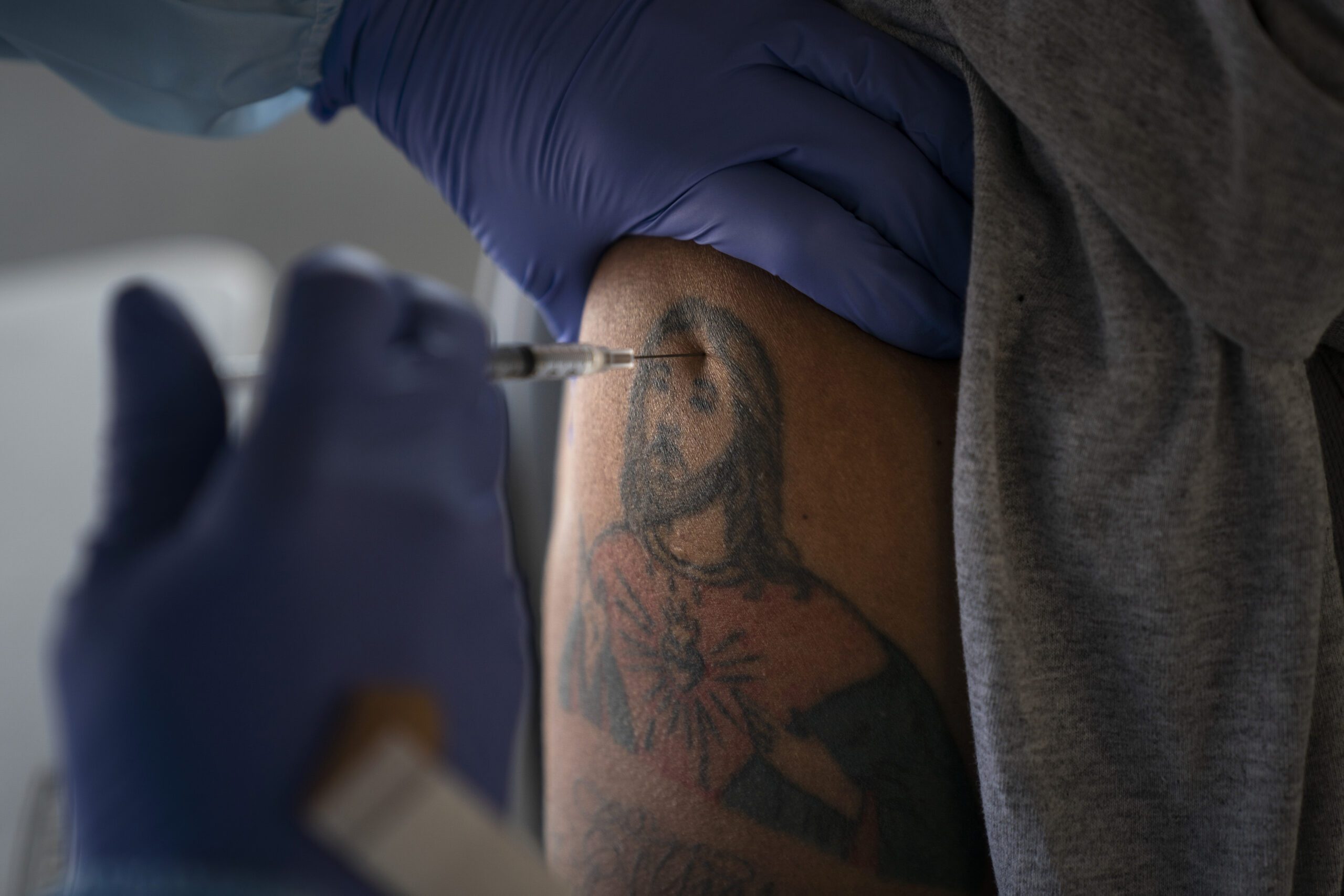 A farm worker receives a dose of a COVID-19 vaccine on his arm his arm bearing a tattoo depicting Jesus.