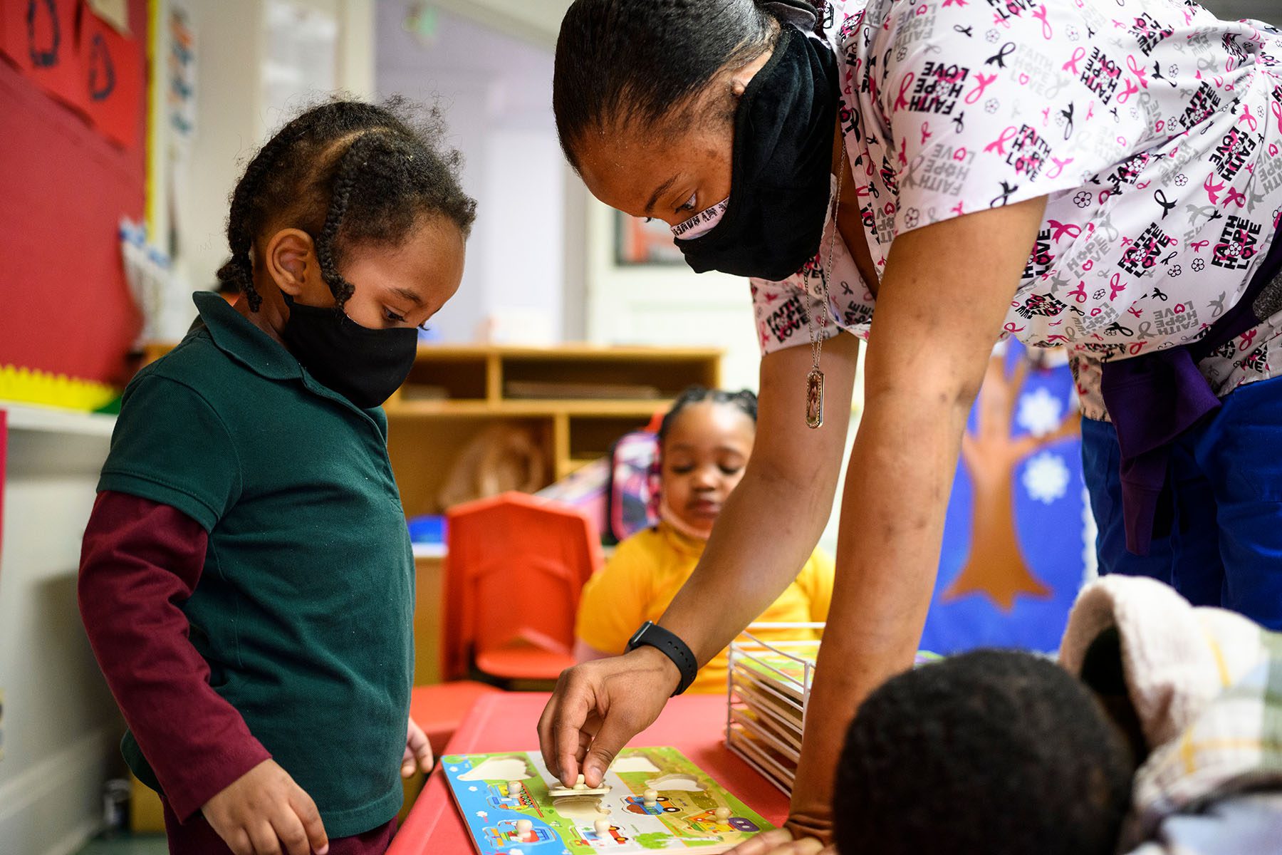 A teacher helps a child solve a puzzle at a daycare.