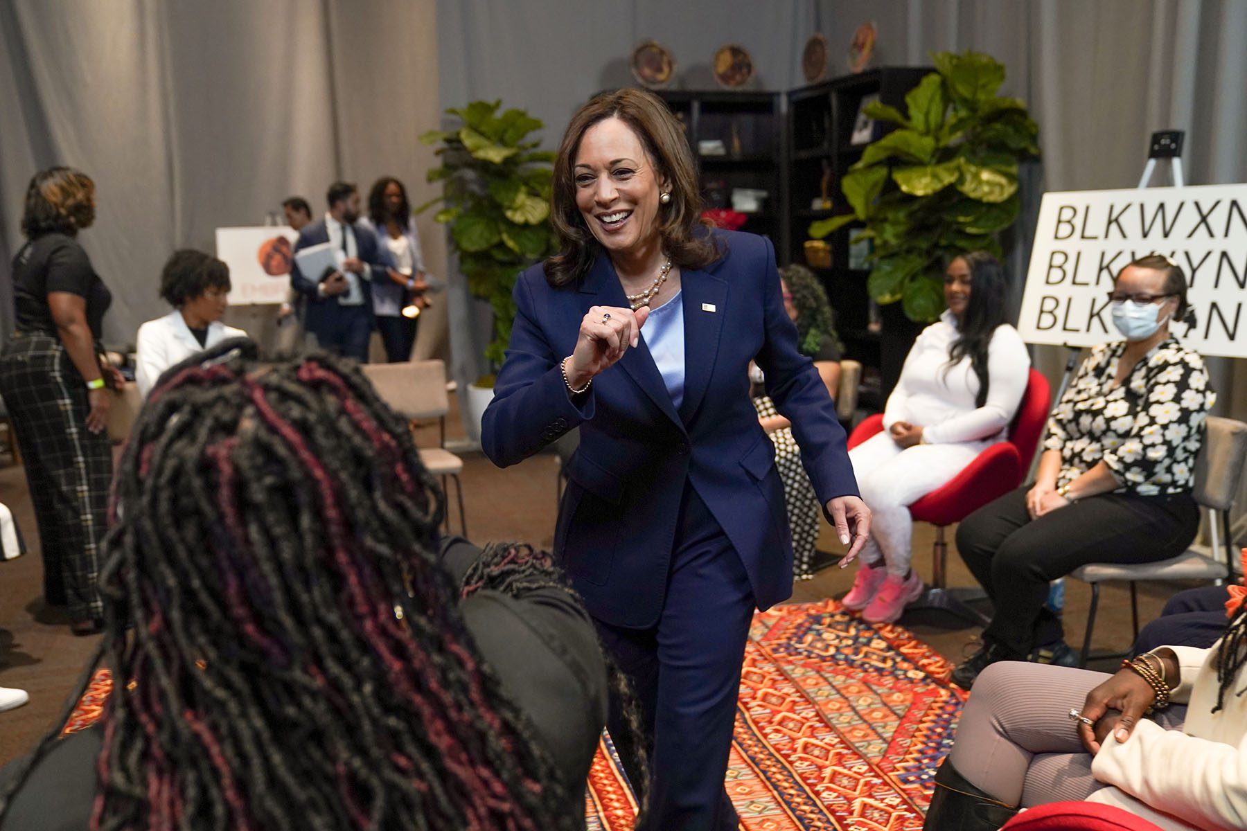 Harris smiles as she gives somebody an elbow bump as others black women sit in chair in a circle.