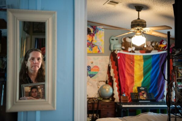 Christine Leinonen clutches onto one of her favorite photos of her son. She is reflected in a mirror as she looks into Christopher's room, in which can be see a large pride flag.
