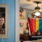 Christine Leinonen clutches onto one of her favorite photos of her son. She is reflected in a mirror as she looks into Christopher's room, in which can be see a large pride flag.