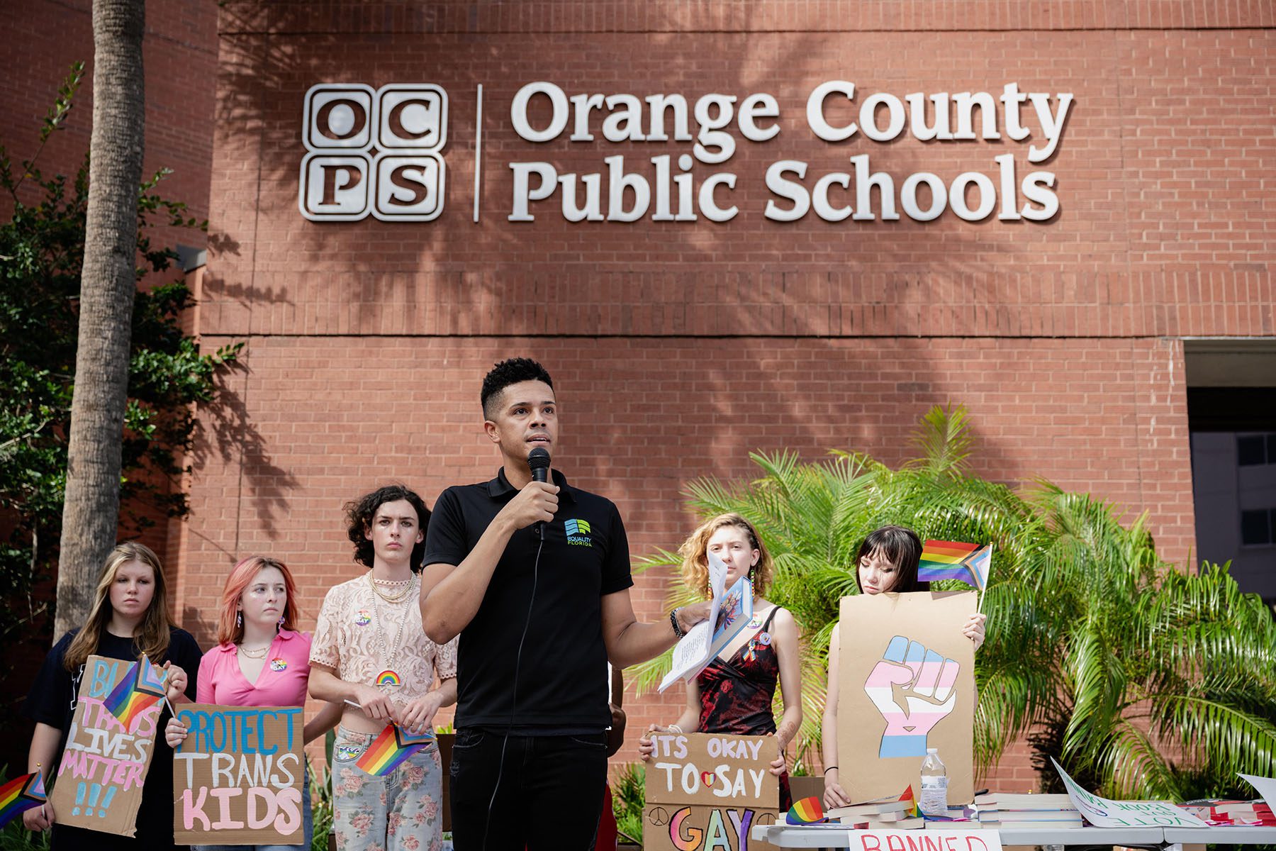 Brandon Wolf speaks outside the Orange County Public Schools board meeting. Behind him, teenagers hold signs that read "It's okay to say gay," "protect trans kids" and "black trans lives matter."