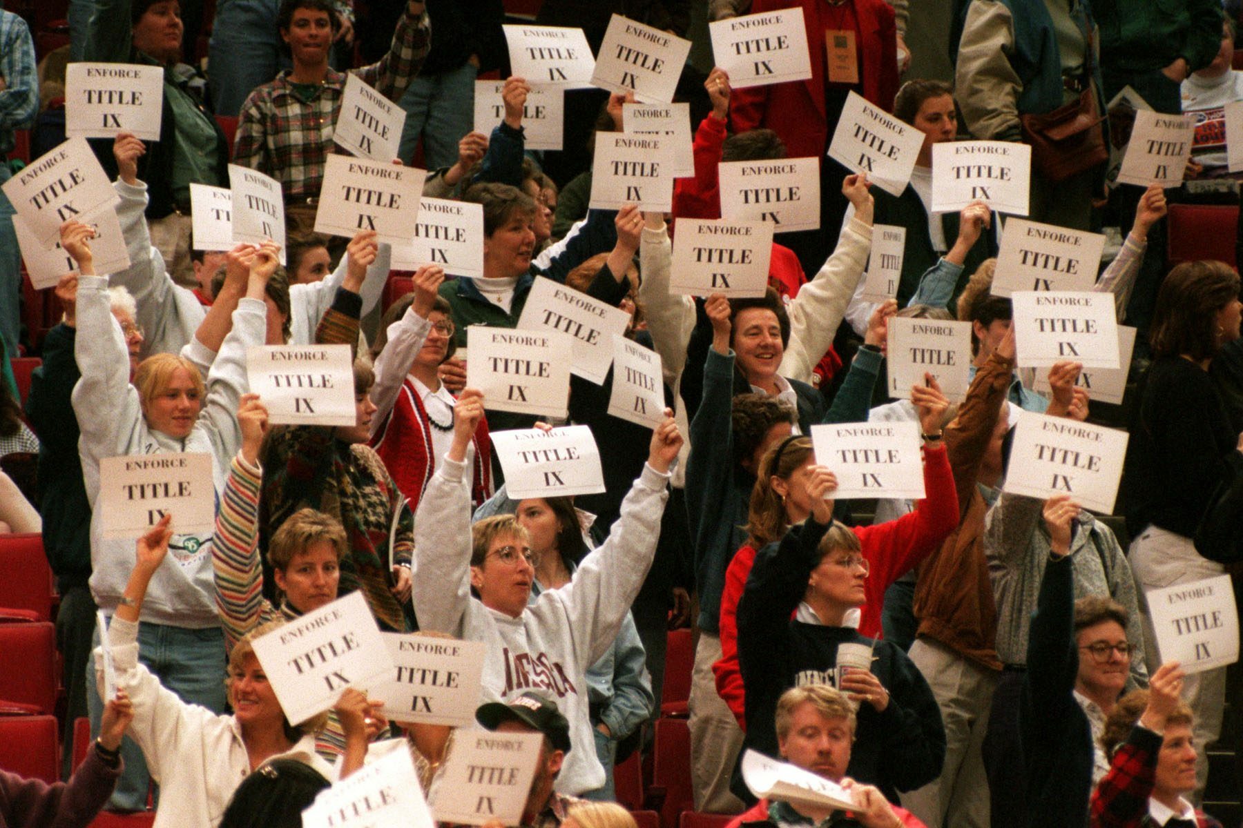 Members and supporters of the Women's Basketball Coaches Association demonstrate in support of Title IX by holding up printed signs that read 