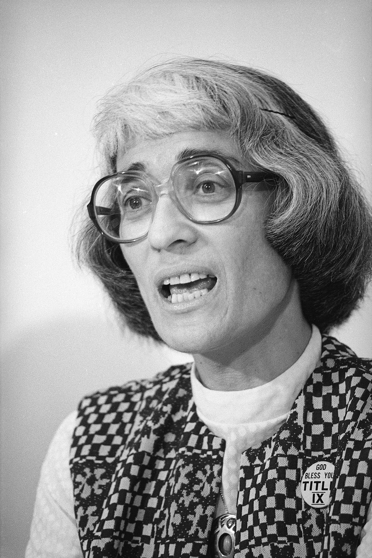 Portrait of Bernice Sandler, she wears a pin that reads "god bless you Title IX" on her vest.