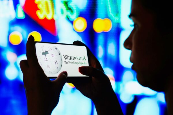 In this photo illustration, a silhouetted woman holds a smartphone with the Wikipedia logo displayed on the screen.