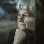A pensive older woman looking out a window.