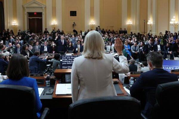 View of committee hearing room, from behind members, with Liz Cheney standing to deliver the oath